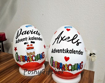 May include: Two white, egg-shaped Advent calendars with red and colorful accents. One says "Davids Adventskalender" with a Santa Claus graphic, the other says "Axels Adventskalender". Both have "Überraschung" written on them.