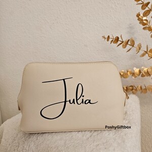 May include: A cream-colored cosmetic bag with a black cursive font that reads "Julia" and the text "PoshyGiftbox" in the bottom right corner.