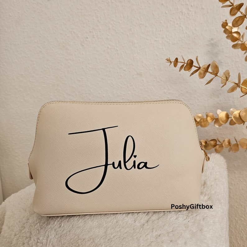 May include: A cream-colored cosmetic bag with a black cursive font that reads "Julia" and the text "PoshyGiftbox" in the bottom right corner.
