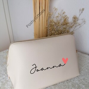May include: A cream-colored zippered makeup bag with the name "Joanna" written in black cursive script and a pink heart.