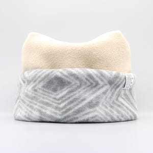 May include: A soft, two-toned fleece pet bed. The top section is a light beige color, and the bottom section is gray with a white geometric pattern. The bed is designed to provide comfort and support for pets.