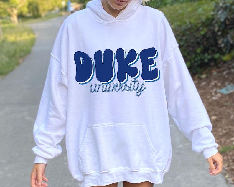 May include: White hoodie with a blue graphic that says "DUKE university" in a retro font.