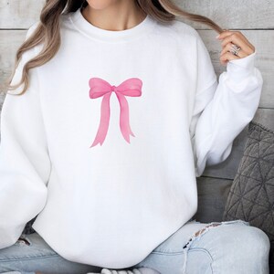 May include: White sweatshirt with a pink watercolor bow design.