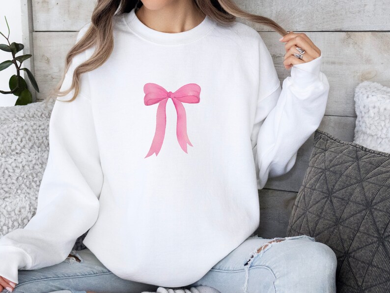 May include: White sweatshirt with a pink watercolor bow design.