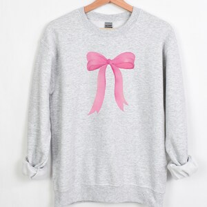 May include: A gray sweatshirt with a pink watercolor bow design.