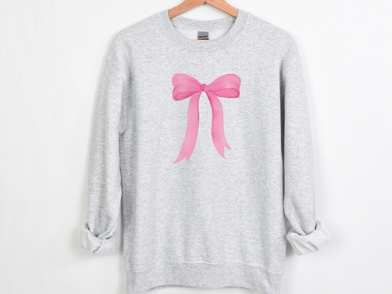 May include: A gray sweatshirt with a pink watercolor bow design.