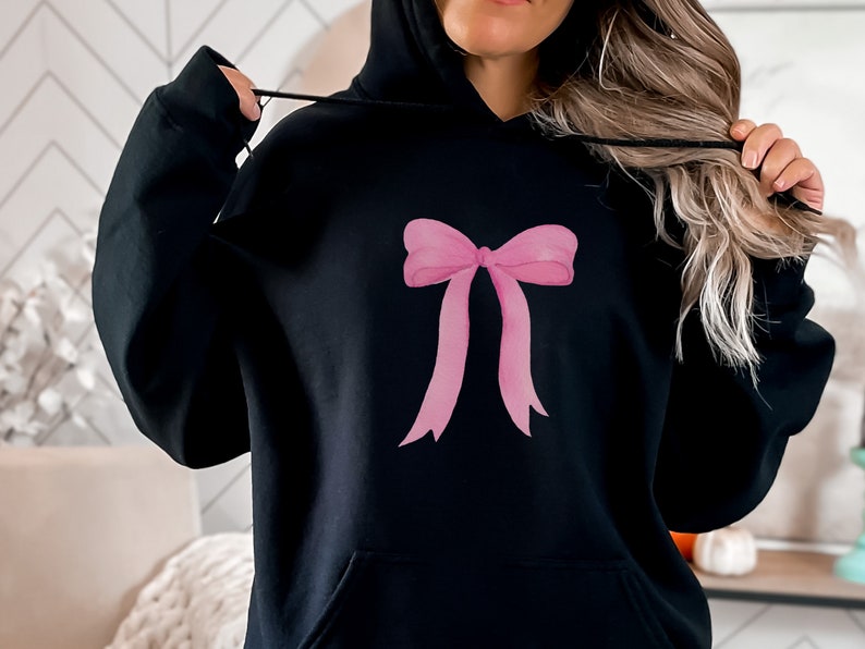 May include: Black hoodie with a pink bow design on the front.