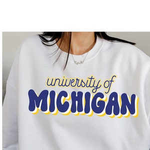May include: White sweatshirt with a blue and yellow graphic that says "university of MICHIGAN" in a retro font.
