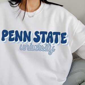 May include: White sweatshirt with a blue and white retro-style graphic that says "Penn State University".