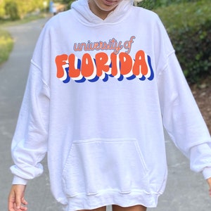 May include: White hoodie with a blue and orange graphic that says "university of FLORIDA" in a retro font.