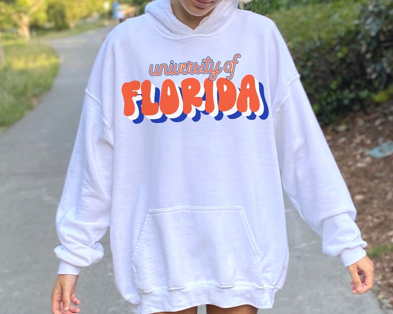 May include: White hoodie with a blue and orange graphic that says "university of FLORIDA" in a retro font.