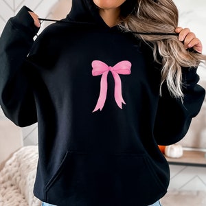 May include: Black hooded sweatshirt with a pink bow design on the front.