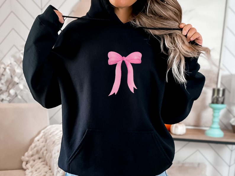 May include: Black hooded sweatshirt with a pink bow design on the front.