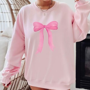 May include: A pink sweatshirt with a large pink watercolor bow printed on the front.