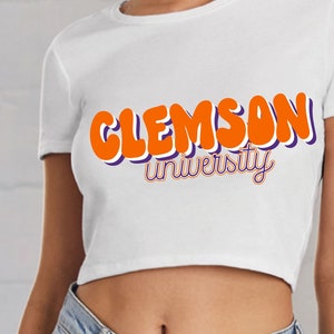 May include: White fitted crop top with the text "Clemson University" in orange and purple lettering.