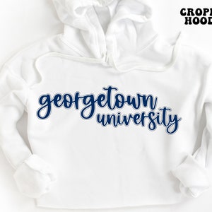 May include: White cropped hoodie with the text "georgetown university" in navy blue lettering.
