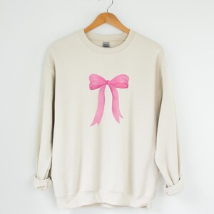 May include: A beige sweatshirt with a pink watercolor bow design.