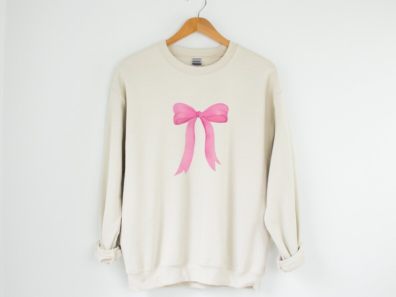 May include: A beige sweatshirt with a pink watercolor bow design.