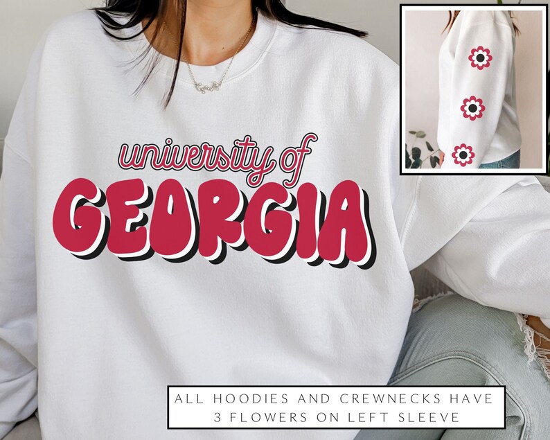 May include: White sweatshirt with the text "university of GEORGIA" in red and black lettering. The sweatshirt has three red flowers on the left sleeve.