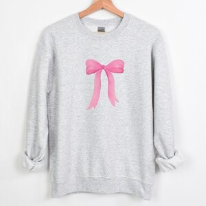 May include: A gray sweatshirt with a pink bow design on the front.