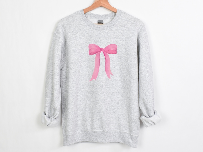 May include: A gray sweatshirt with a pink bow design on the front.