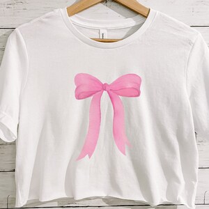 May include: A white cropped t-shirt with a pink watercolor bow design.