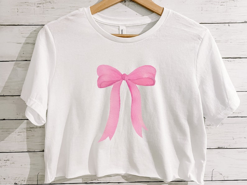 May include: A white cropped t-shirt with a pink watercolor bow design.