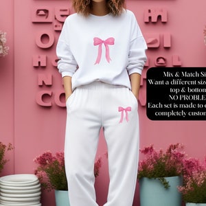 May include: White sweatshirt and sweatpants set with pink bows on the front. The text "Mix & Match Sizing! Want a different size for your top & bottom? NO PROBLEM! Each set is made to order and completely customizable." is on the right side of the image.