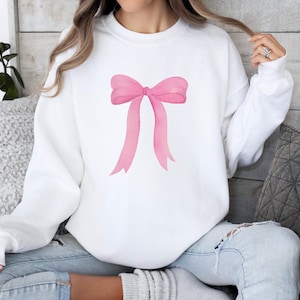 May include: A white sweatshirt with a pink watercolor bow design.