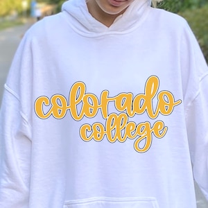 May include: White hoodie with a yellow and black graphic that says "Colorado College" in a handwritten font.