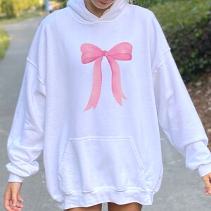 May include: White oversized hoodie with a pink bow graphic on the front.