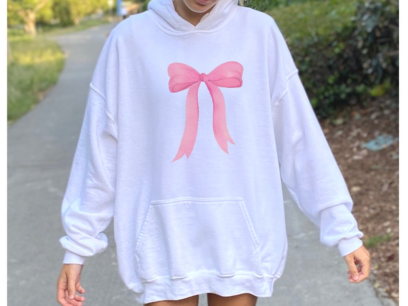 May include: White oversized hoodie with a pink bow graphic on the front.