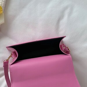Puede incluir: Un bolso de hombro de piel sint&eacute;tica rosa con cierre dorado y forro negro. El bolso est&aacute; abierto y el interior es visible.