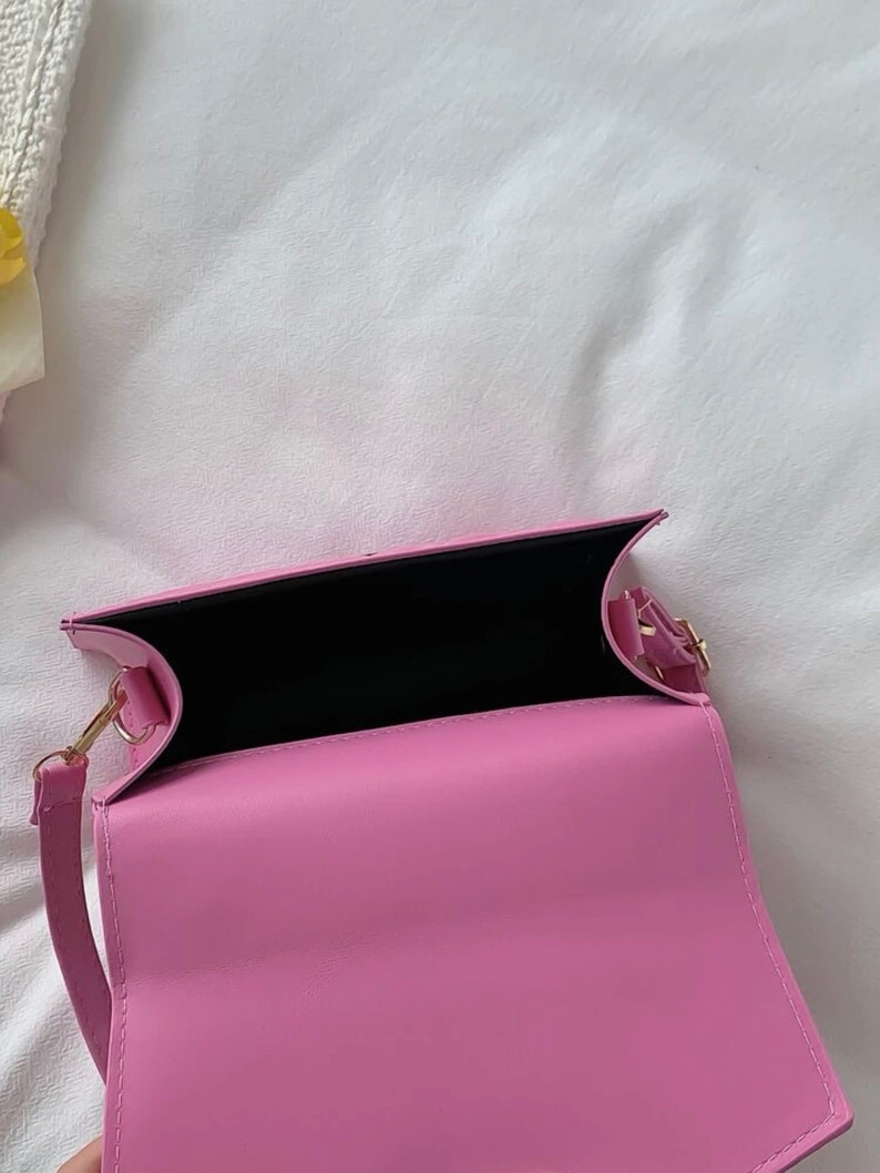 Puede incluir: Un bolso de hombro de piel sint&eacute;tica rosa con cierre dorado y forro negro. El bolso est&aacute; abierto y el interior es visible.