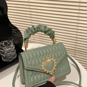 Puede incluir: Un bolso de mano verde acolchado con un cierre dorado en forma de coraz&oacute;n y una correa de cadena.