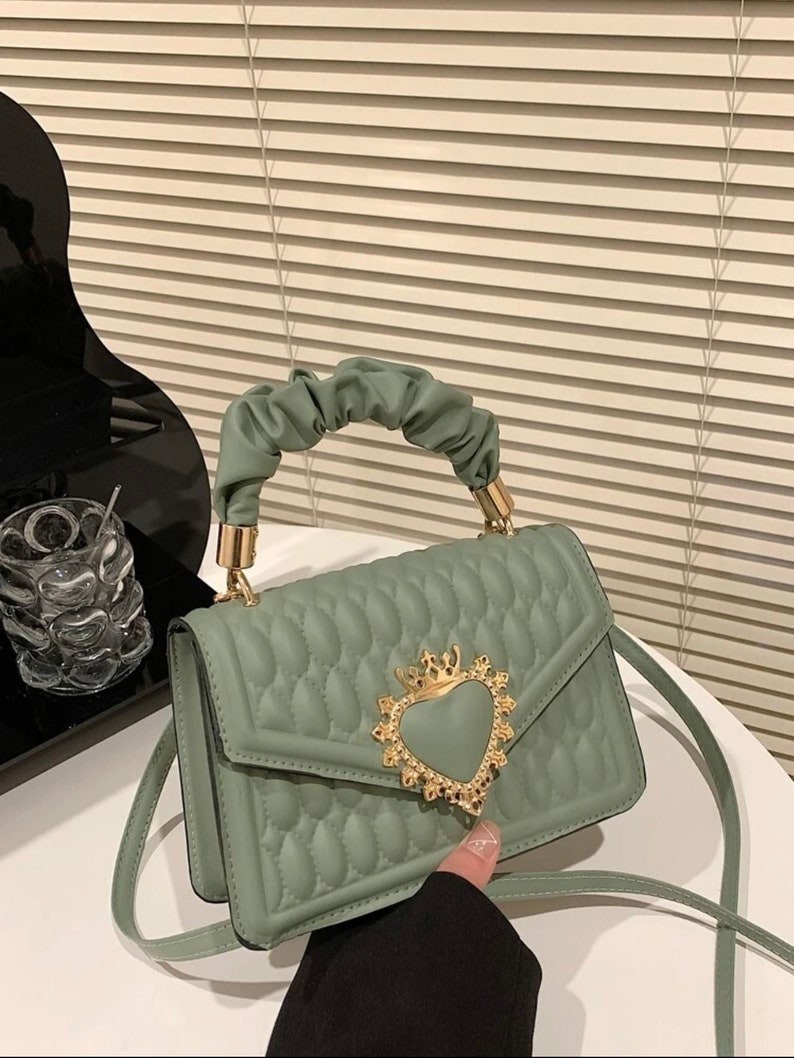 Puede incluir: Un bolso de mano verde acolchado con un cierre dorado en forma de coraz&oacute;n y una correa de cadena.