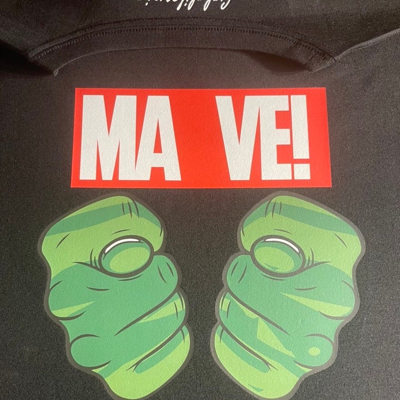May include: Black t-shirt with a red rectangle that says "MA VE!" and two green fists on either side.