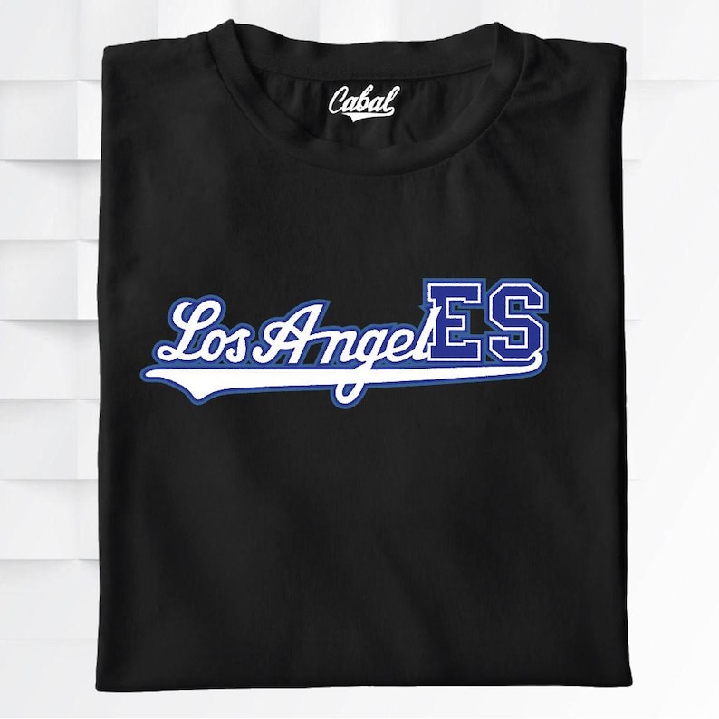 May include: Black t-shirt with the text "Los Angeles" in a white script font with a blue outline, and the letters "ES" in a blue block font. The brand name "Cabal" is printed on the collar.