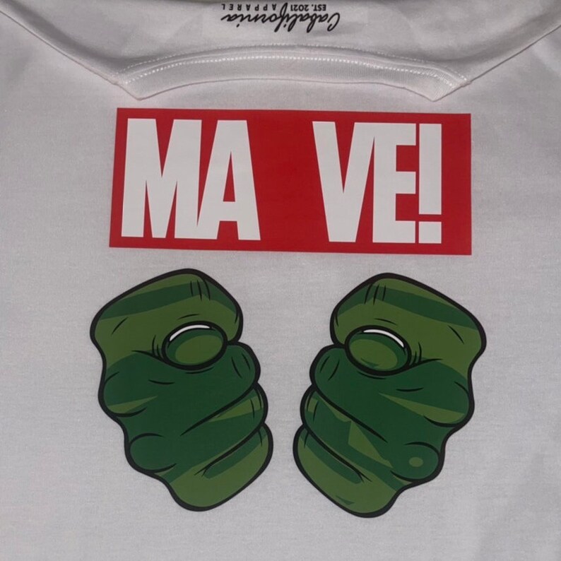 May include: White t-shirt with a red rectangle that says "MA VE!" and two green fists with white knuckles.