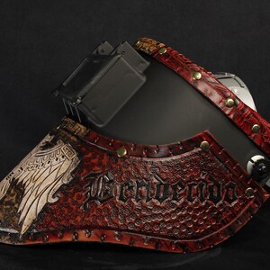 Op de afbeelding: Een zwart en rood leren masker met het woord "Benvendo" in reli&euml;f op de voorkant. Het masker heeft een gedetailleerd ontwerp met klinknagels en een vogelafbeelding. Het masker is waarschijnlijk voor cosplay of kostuums.