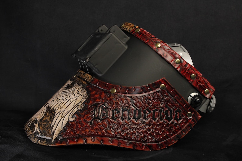 Op de afbeelding: Een zwart en rood leren masker met het woord "Benvendo" in reli&euml;f op de voorkant. Het masker heeft een gedetailleerd ontwerp met klinknagels en een vogelafbeelding. Het masker is waarschijnlijk voor cosplay of kostuums.