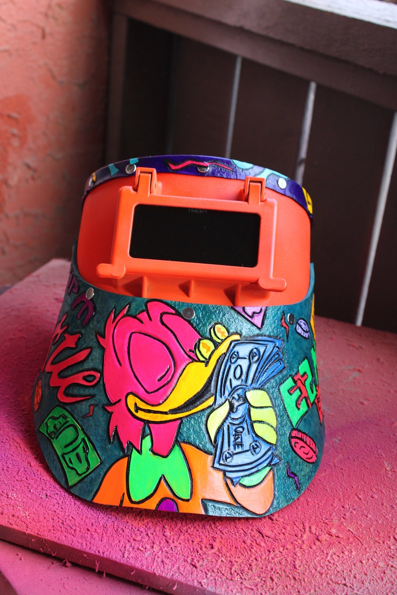 May include: A bright orange welding helmet with a dark visor. The helmet is decorated with a cartoon duck holding money, and the words "Get Rich" and "Club" are written on the side.