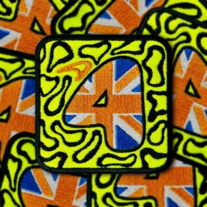 Può includere: Una toppa ricamata gialla e nera con un design Union Jack all'interno del numero 4. La toppa ha un bordo nero e uno sfondo giallo con linee nere ondulate.
