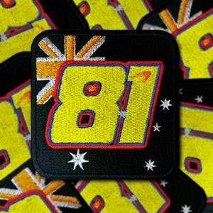 Puede incluir: Un parche bordado negro con un número amarillo "81" rodeado por un borde rojo, azul y blanco. El número se coloca sobre un fondo de una explosión de estrellas blanca y naranja con un diseño de bandera del Reino Unido.
