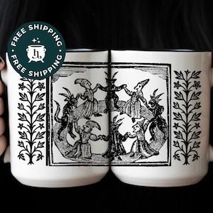 May include: Two white ceramic mugs with a black rim and a black and white illustration of figures dancing in a circle. The mugs have a floral design on the sides. A round sticker with the words "FREE SHIPPING" is visible.