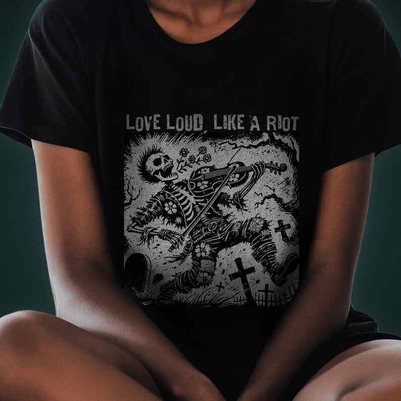 A Folk Punk Linocut shirt with a black and white image of a crust punk Skeleton playing the fiddle in a graveyard. These Offensive T-Shirts have the words Love Loud, Like A Riot; at the top.
