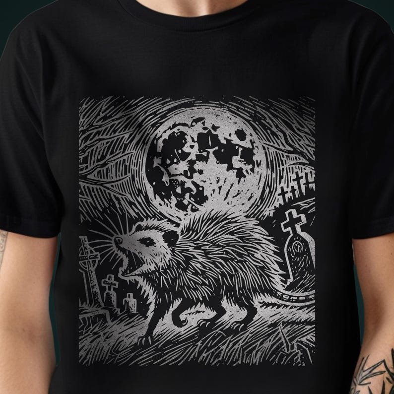 A folk punk linocut shirt with a black and white image of a crust punk opossum howling at the moon in a graveyard. Awesome opossum shirt for alt clothing folks