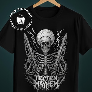 Puede incluir: Camiseta negra con un diseño gráfico blanco detallado de un esqueleto sosteniendo dos espadas, con una forma grande similar a un ojo detrás del cráneo. El texto "THEY/THEM MAYHEM" se muestra debajo en una fuente estilizada.