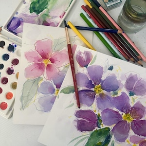 Op de afbeelding: Aquarel schilderijen van bloemen in roze en paarse tinten, met groene bladeren. Een penseel en kleurpotloden liggen naast de schilderijen. Aquarelpaletten en een pot zijn ook zichtbaar.