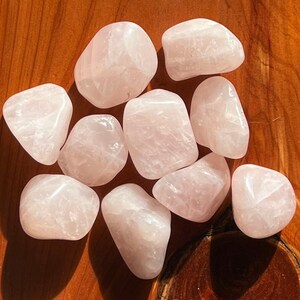 May include: A collection of ten tumbled rose quartz stones. The stones are a pale pink color and have a smooth, polished finish.